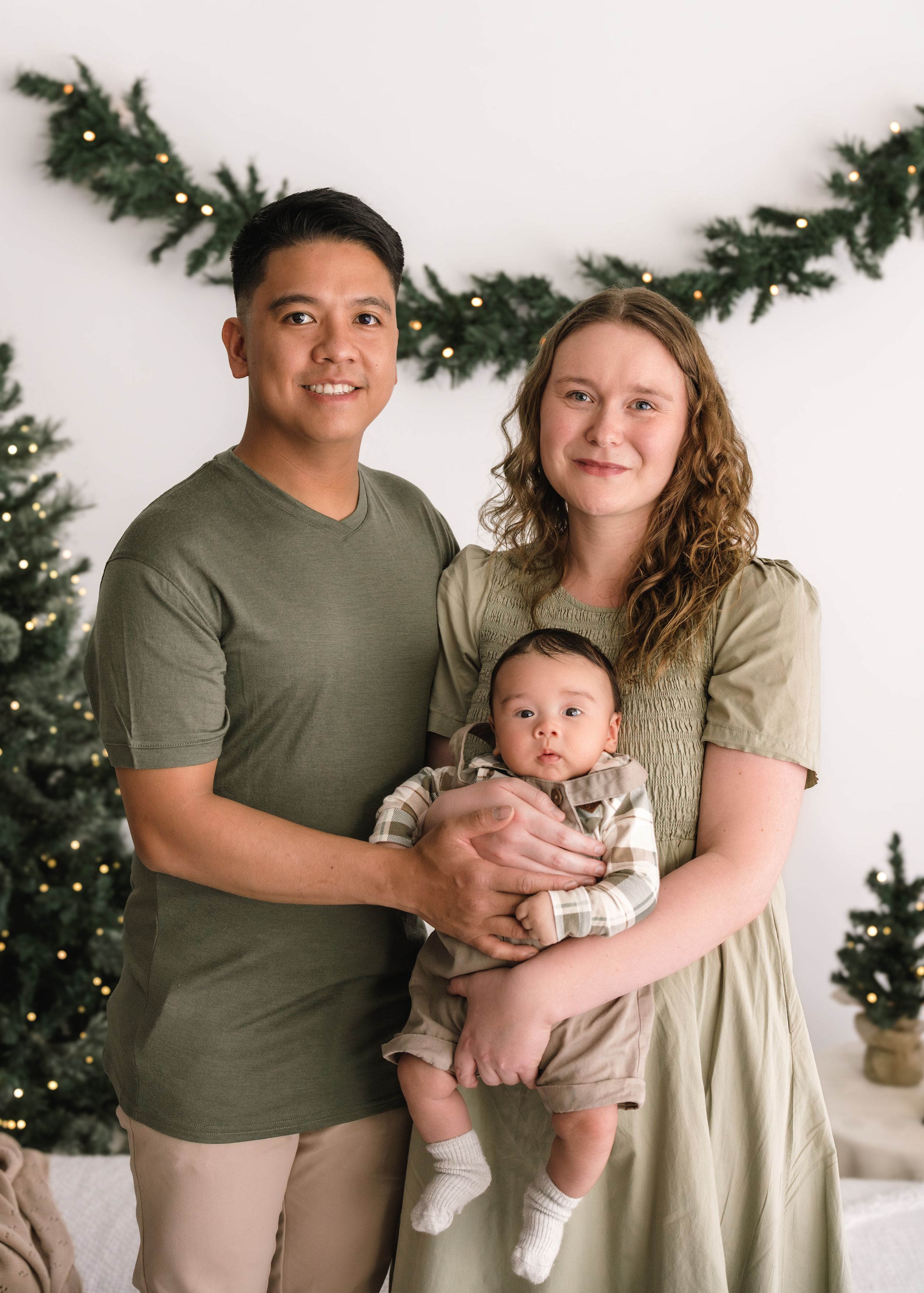 A couple poses together with a baby in front of a Christmas tree in a series of four connected photos.