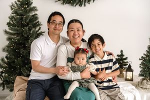A family poses together in front of Christmas trees in a series of holiday portrait photos.