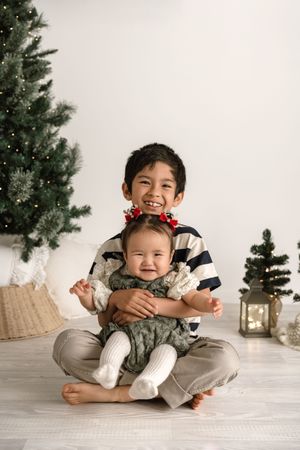 Five sequential holiday photos showing a young child in casual attire posing playfully on a white floor near a Christmas tree.