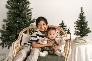 A festive holiday photo session with Christmas trees and wooden chairs arranged in a white studio setting.
