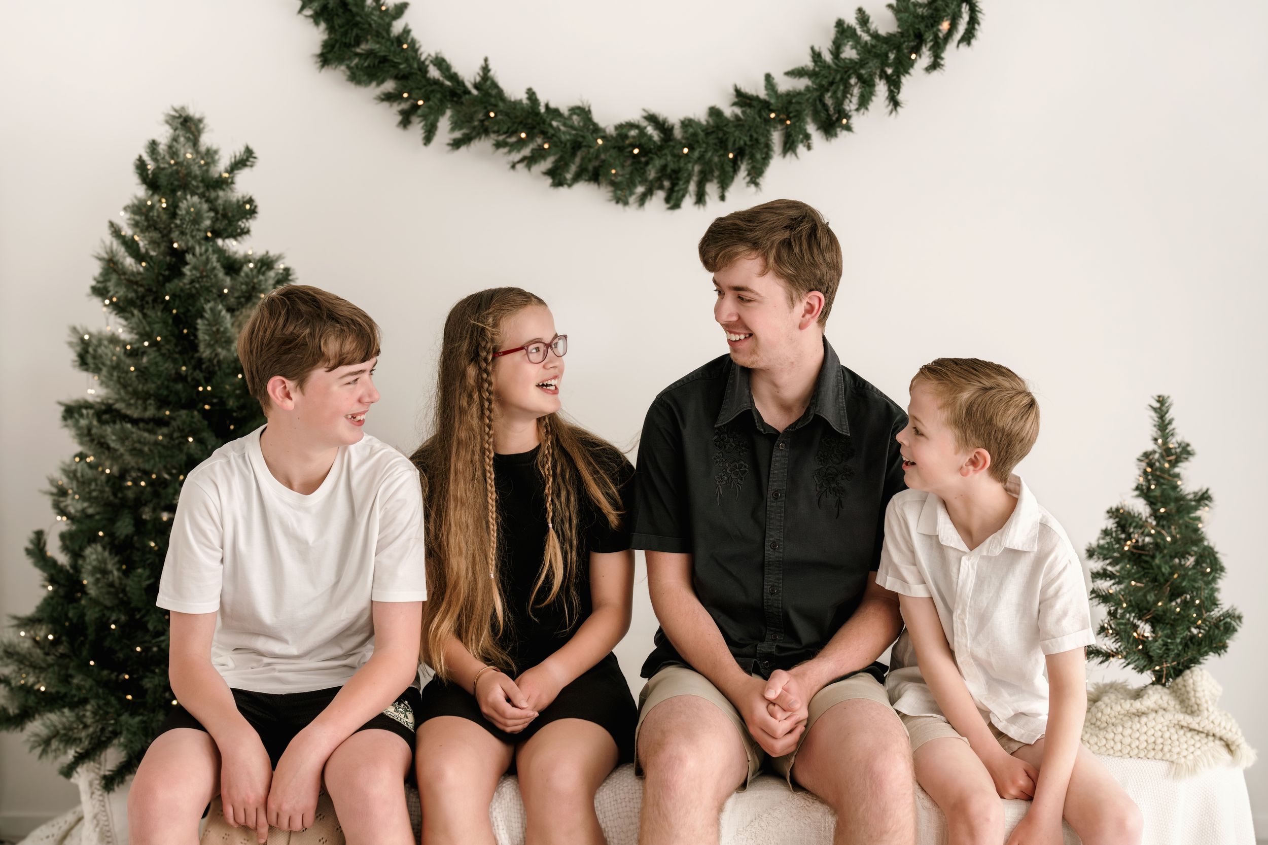 A group sits together on a bench in front of holiday greenery decorations in a casual indoor setting.