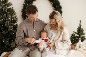 Family sits together near decorated Christmas tree in cozy living room with warm lighting and festive decor.