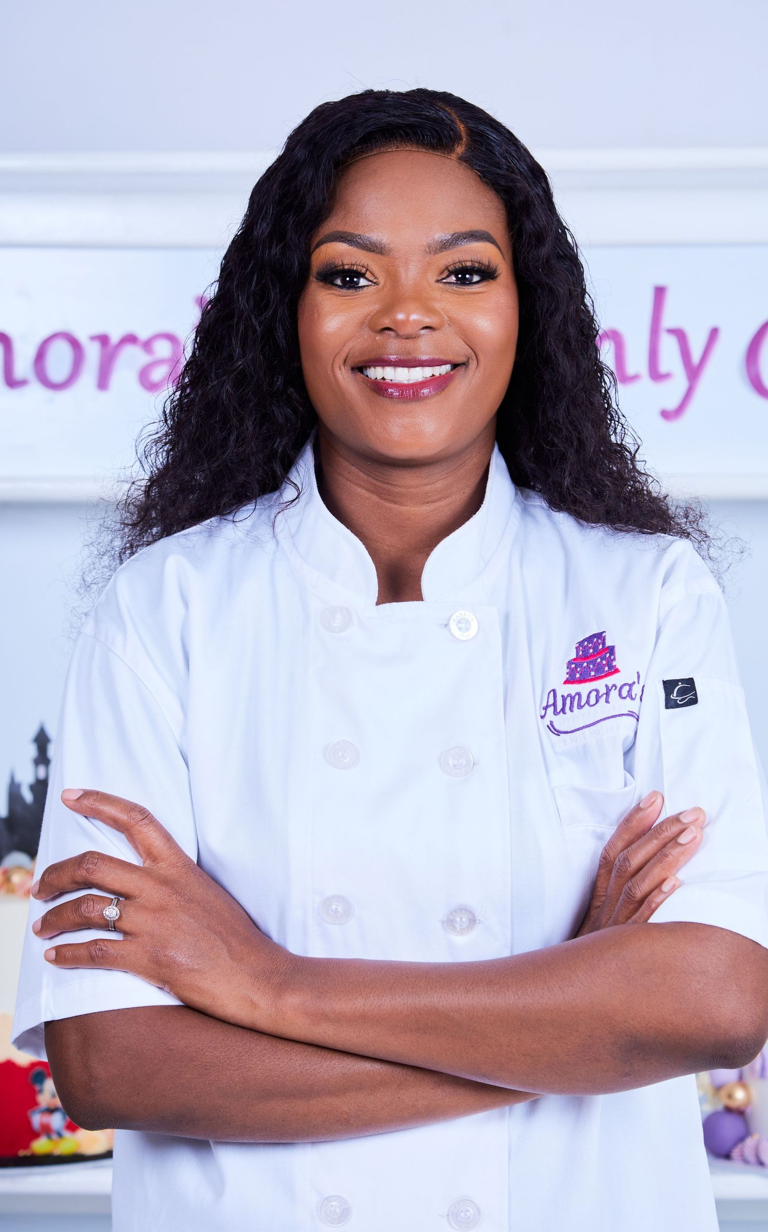 Professional baker in white chef coat smiles confidently with crossed arms.