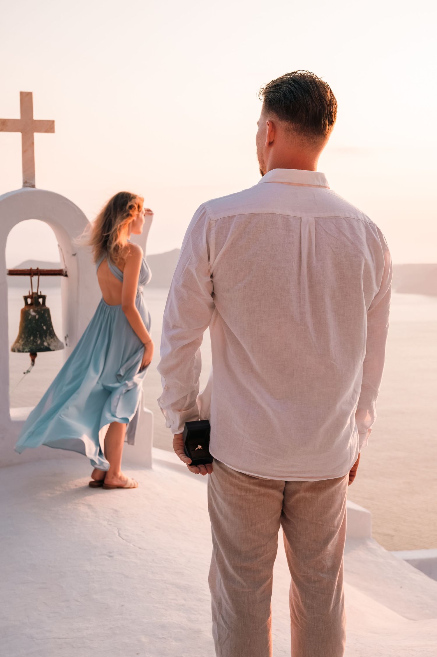 Romantic proposal setup with heart made of red roses overlooking Santorini caldera at sunset.