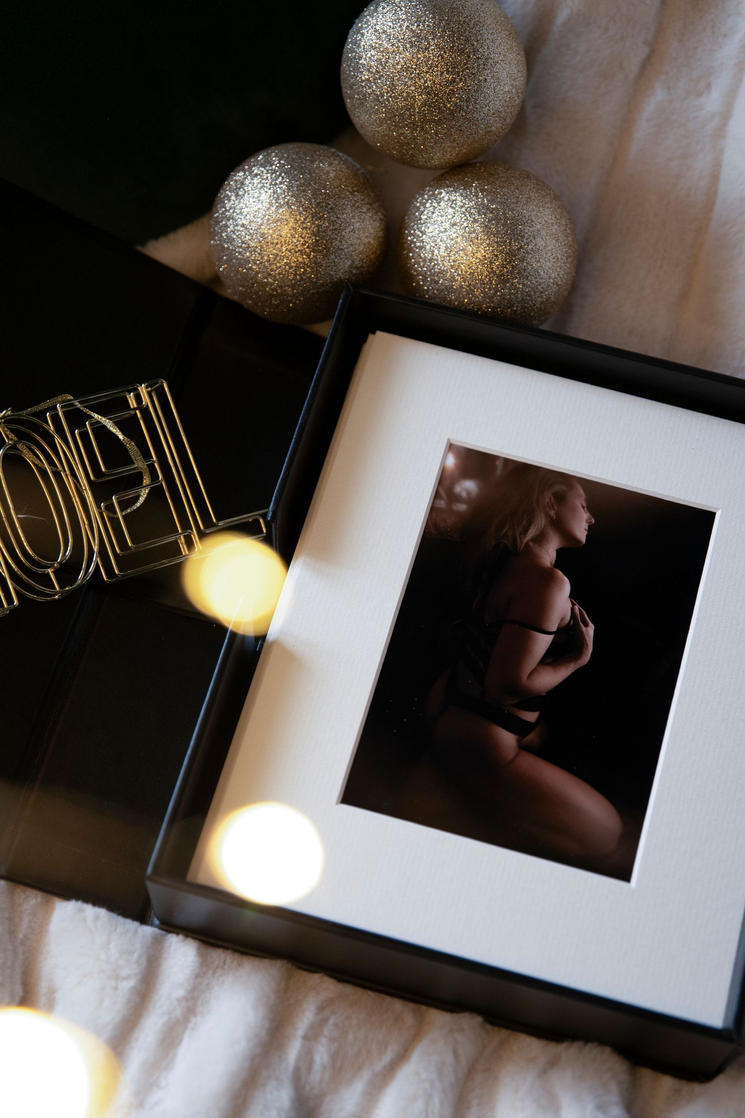 Artistic maternity photograph in frame with silver decorative balls and holiday lights creating an intimate mood.