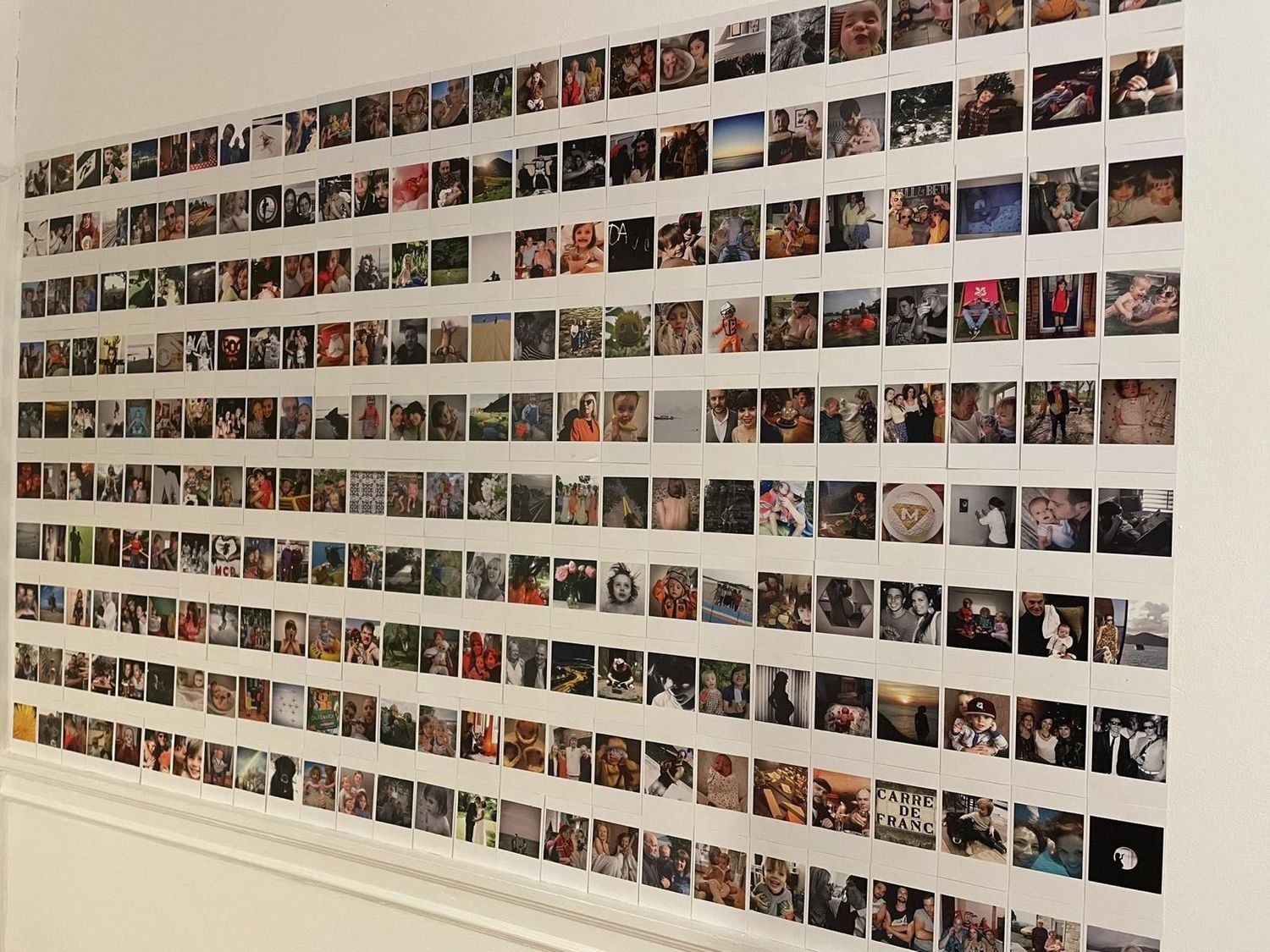 Large photo collage wall display with hundreds of polaroid-style pictures arranged in neat rows.