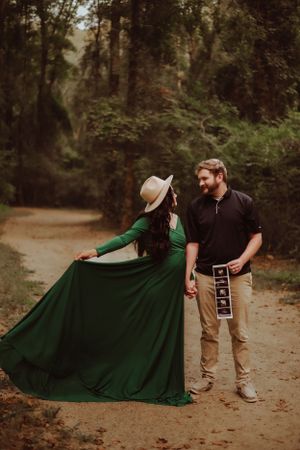 Maternity photo featuring flowing green dress and ultrasound pictures in forest setting.
