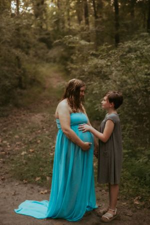 Mother and child share tender moment on forest path during maternity photoshoot.