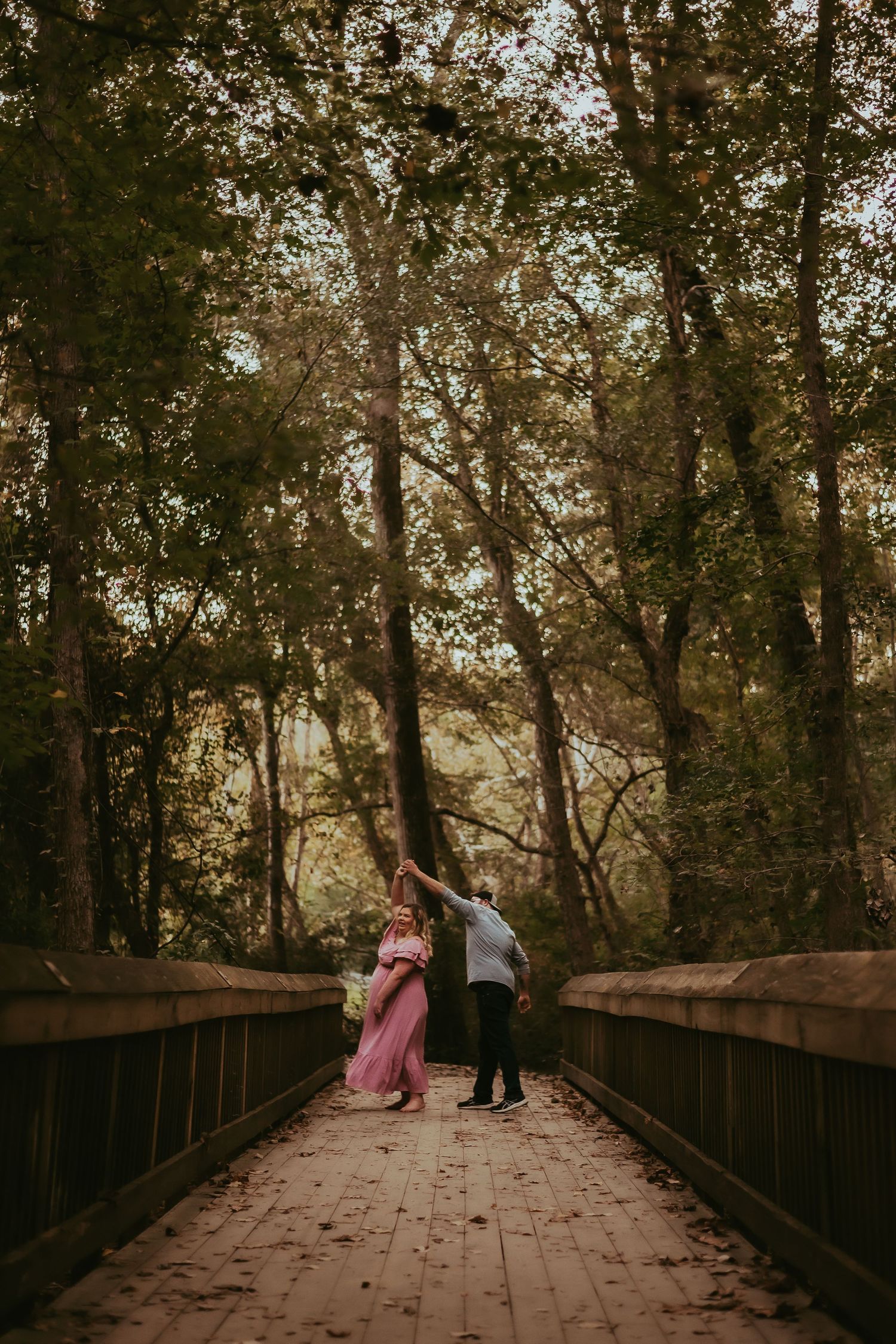 Couple shares intimate moment on wooden bridge in forest setting.