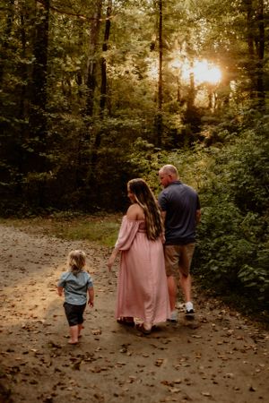Family walks down a sunlit forest path during golden hour.