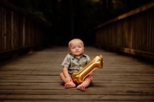 Child sits cross-legged on wooden bridge holding golden balloon.