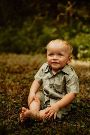 Child sitting in grass wearing gray button-up shirt.