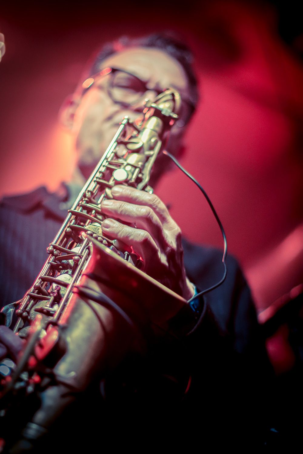 Detailed macro shot of hands playing a saxophone with red lighting.