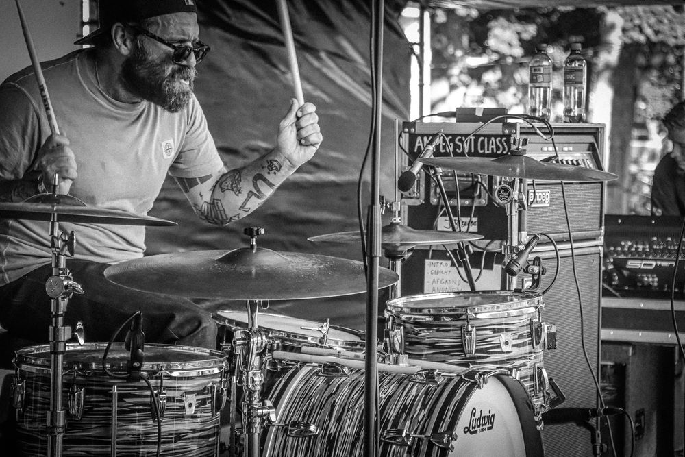 Close-up shot of a drummer performing behind a drum kit in black and white.