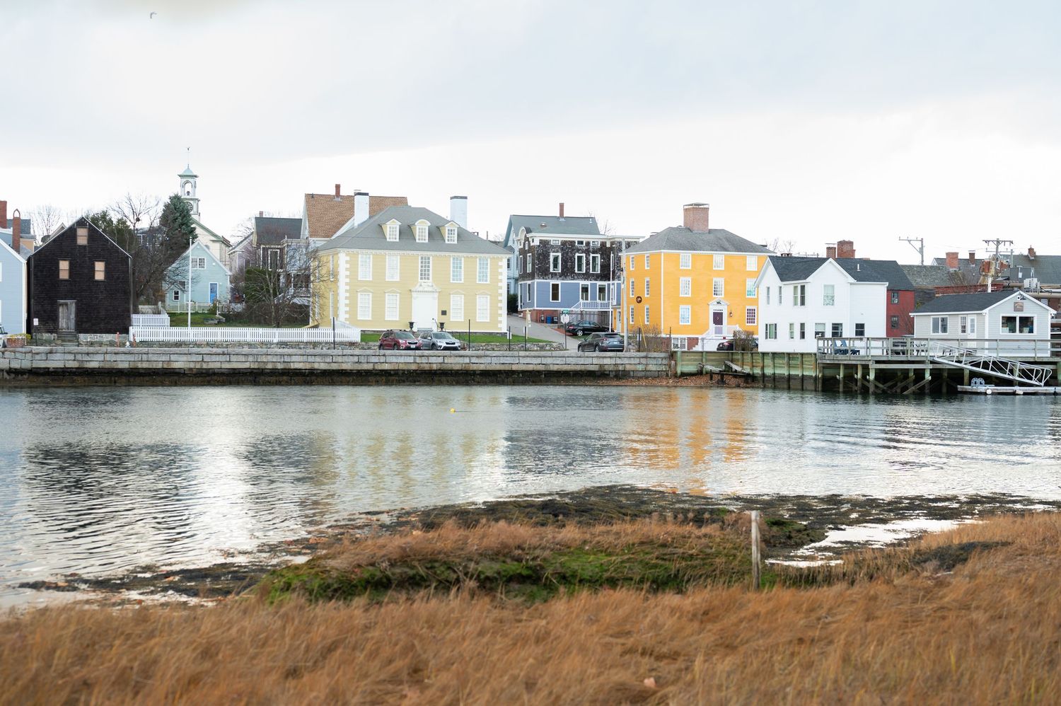 Colorful historic homes line a scenic waterfront in a charming New England coastal town.