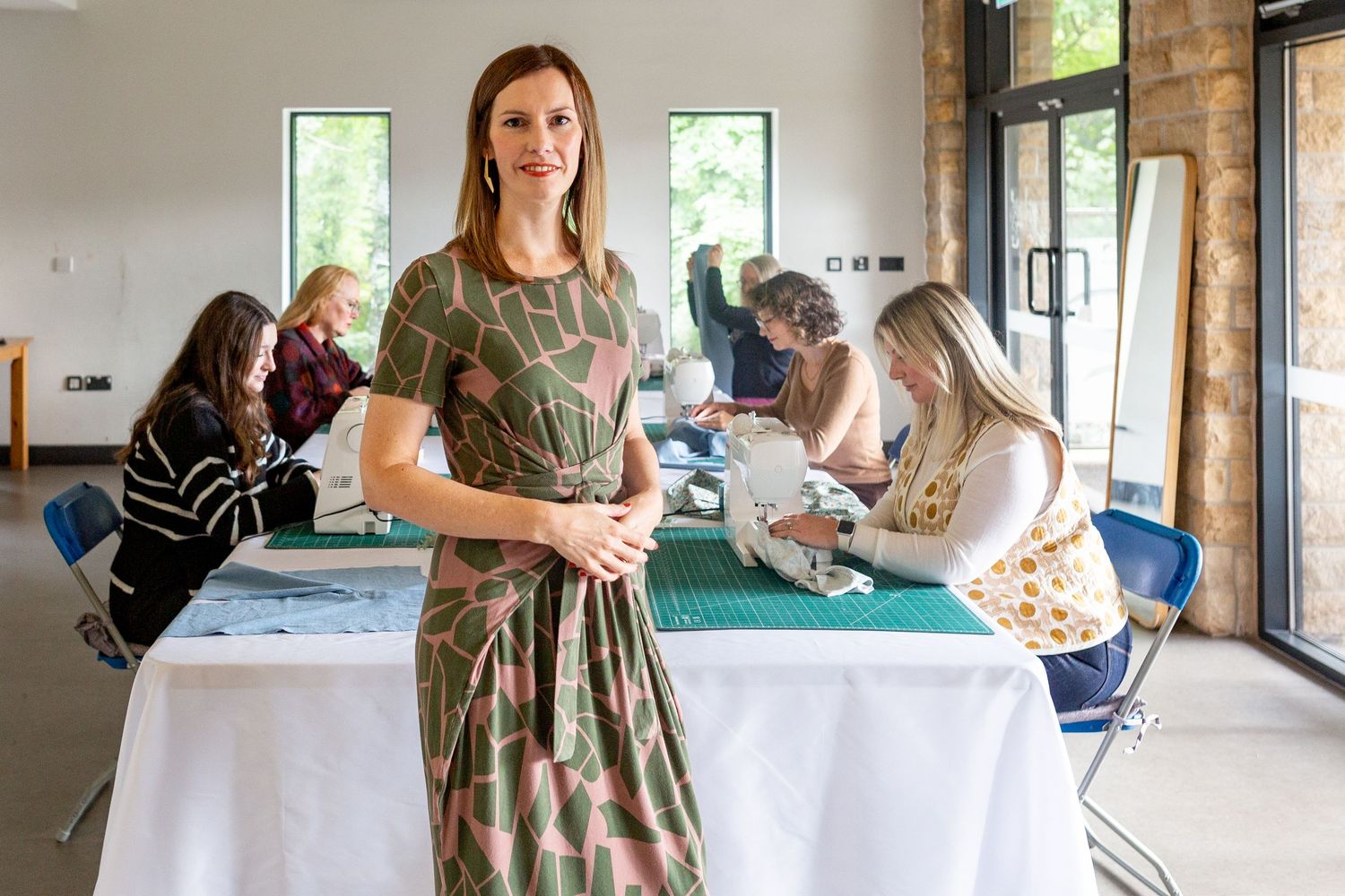 Woman in camo dress stands at event table while others socialize in background.