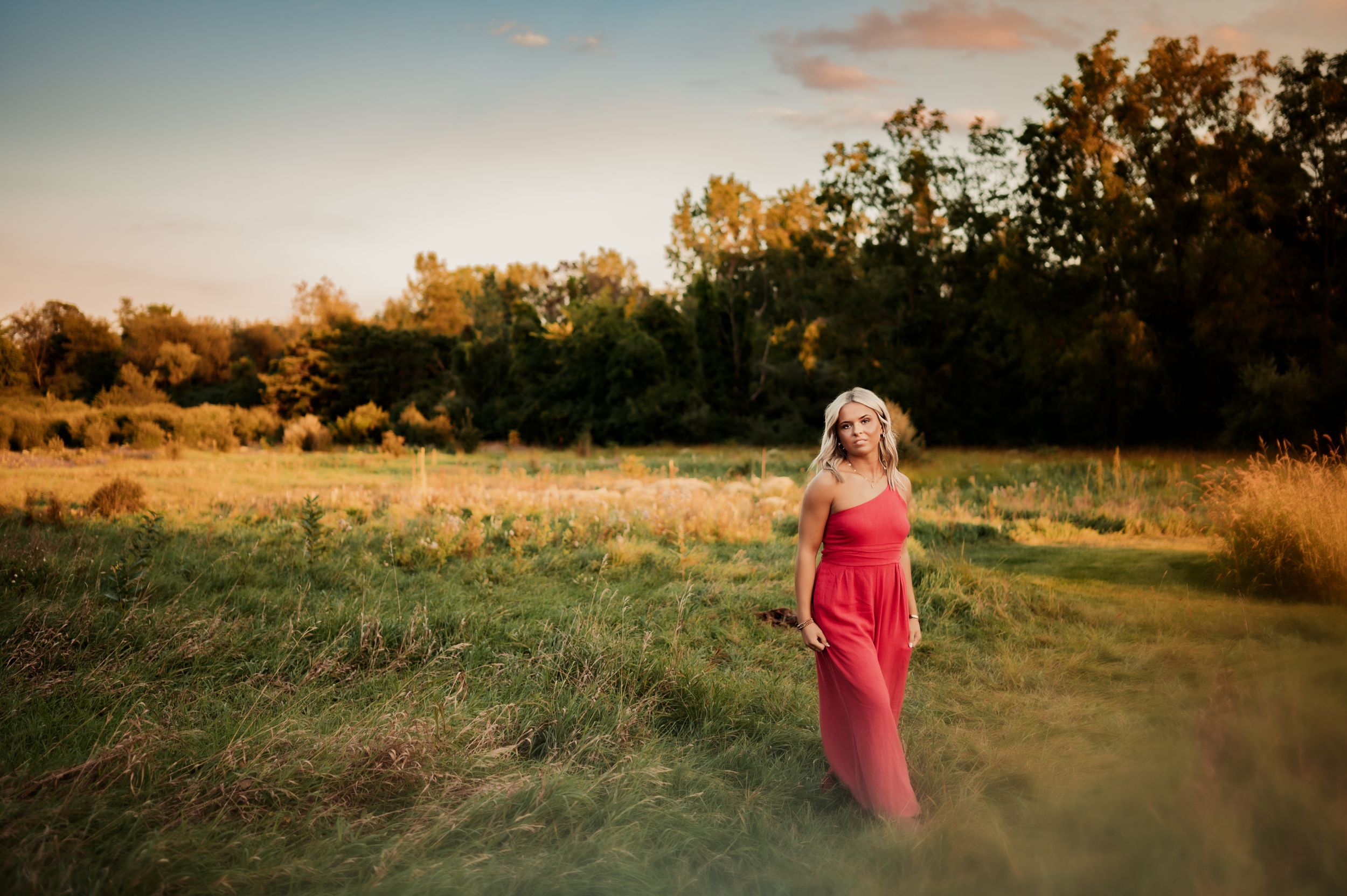 Person in red dress standing in golden field during summer sunset.