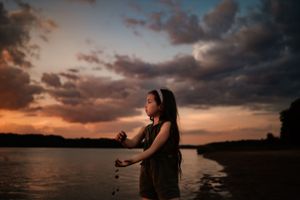 Silhouette of person by lake during dramatic sunset with orange clouds.