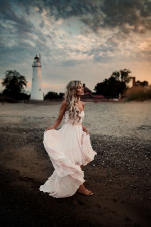 Woman in flowing white dress near lighthouse during dramatic sunset.