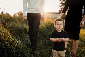 Child standing between two adults in grassy field at sunset.