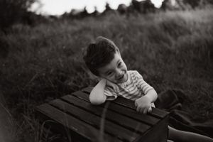 Child resting head on wooden table outdoors in black and white photography.