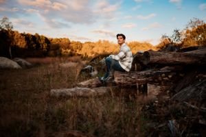 Person sitting on rocks in an autumn field during golden hour with dramatic sunset lighting.