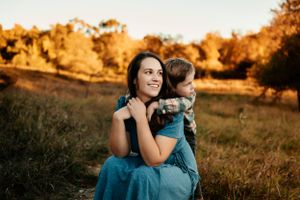 A tender moment between parent and child in a golden autumn field wearing teal blue at sunset.