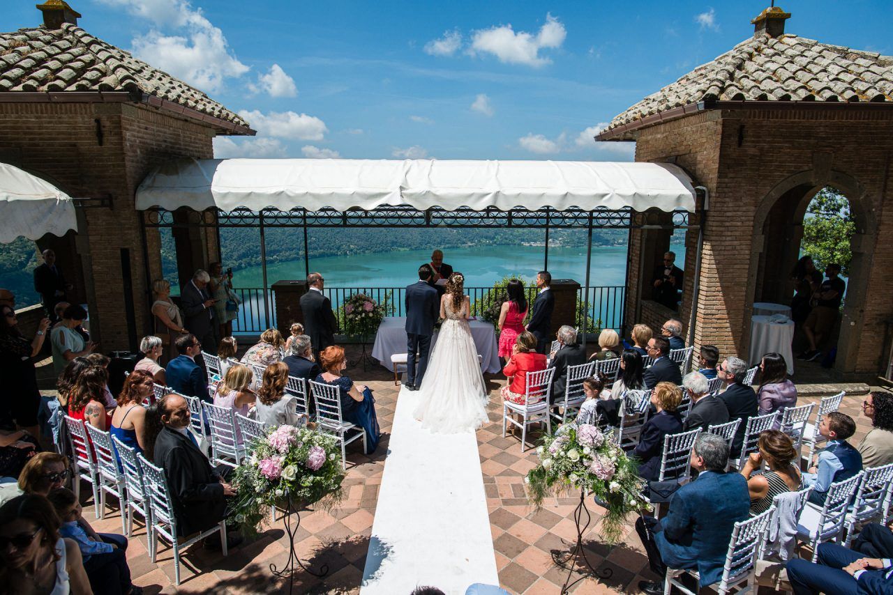 Outdoor wedding ceremony at seaside pavilion with guests seated under blue sky.