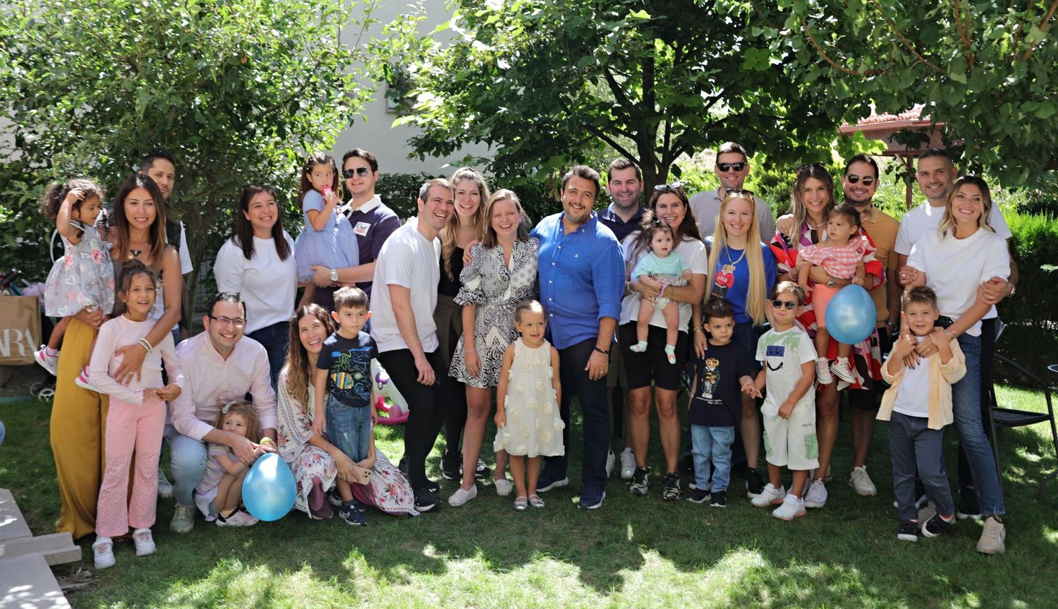 Large extended family gathering for group photo outdoors in summer garden setting.
