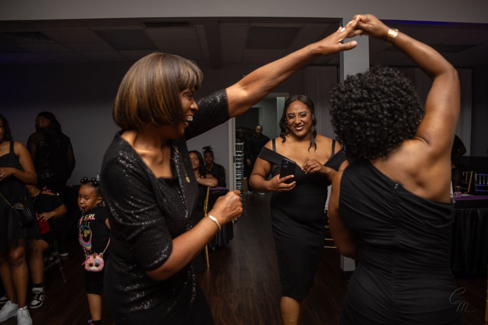 Friends dancing together at a celebration wearing black dresses.