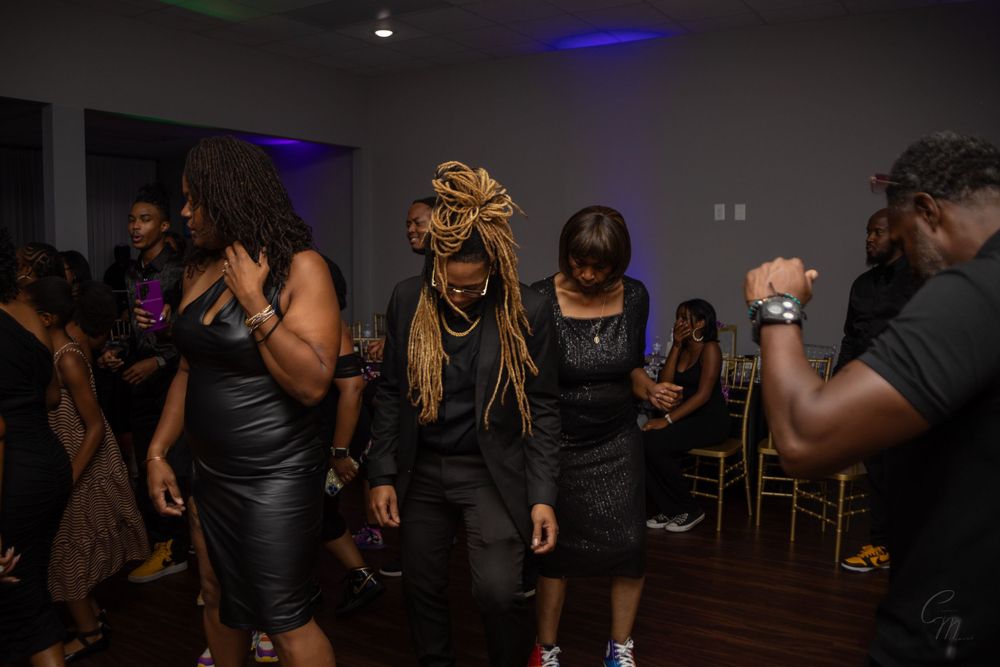 People dancing at a party wearing black outfits under blue lighting.