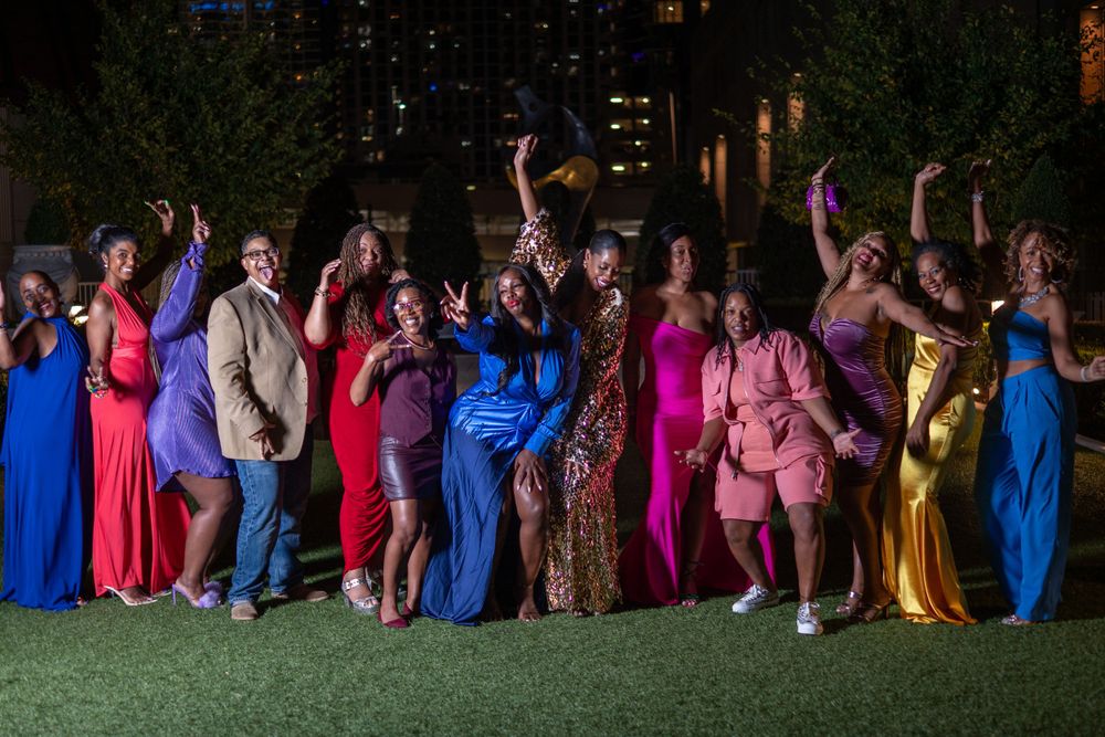 Large group in formal attire poses together on grass at night wearing vibrant dresses.