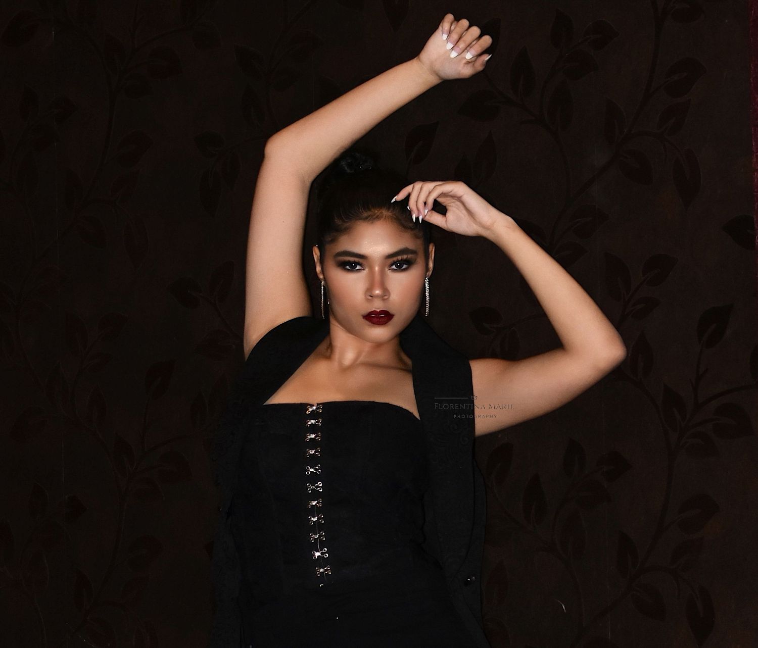 A dramatic fashion portrait in a black corset top with arms raised in a graceful pose.