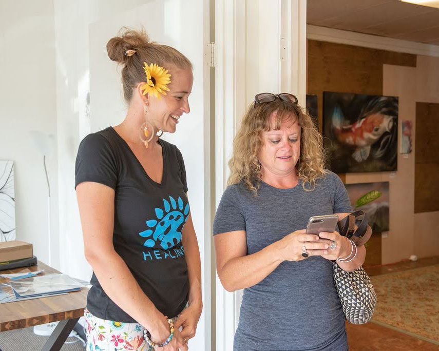 Two people looking at a mobile device in a bright hallway with artwork on the walls.