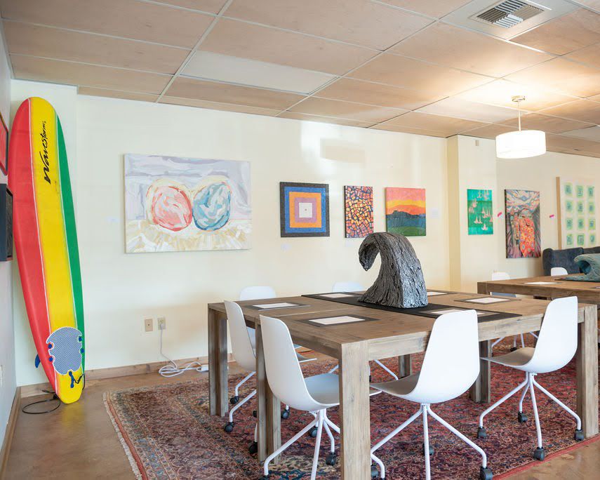 Creative workspace with surfboards, modern chairs, and colorful artwork displayed on white walls.