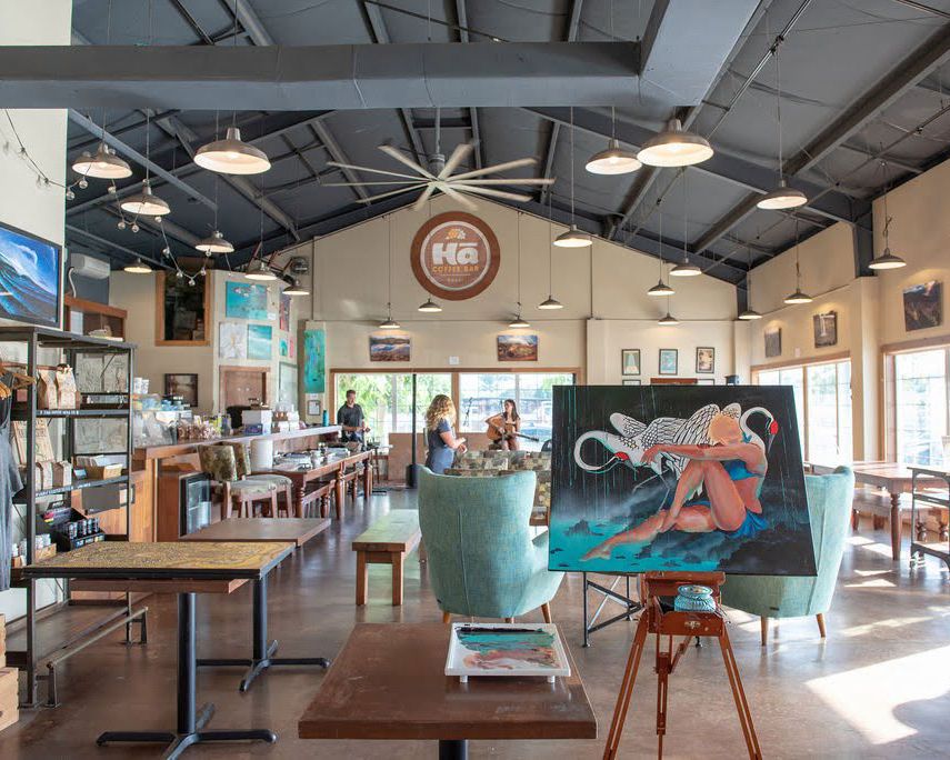 Modern cafe interior with industrial ceiling, mixed seating, and coastal-themed artwork.