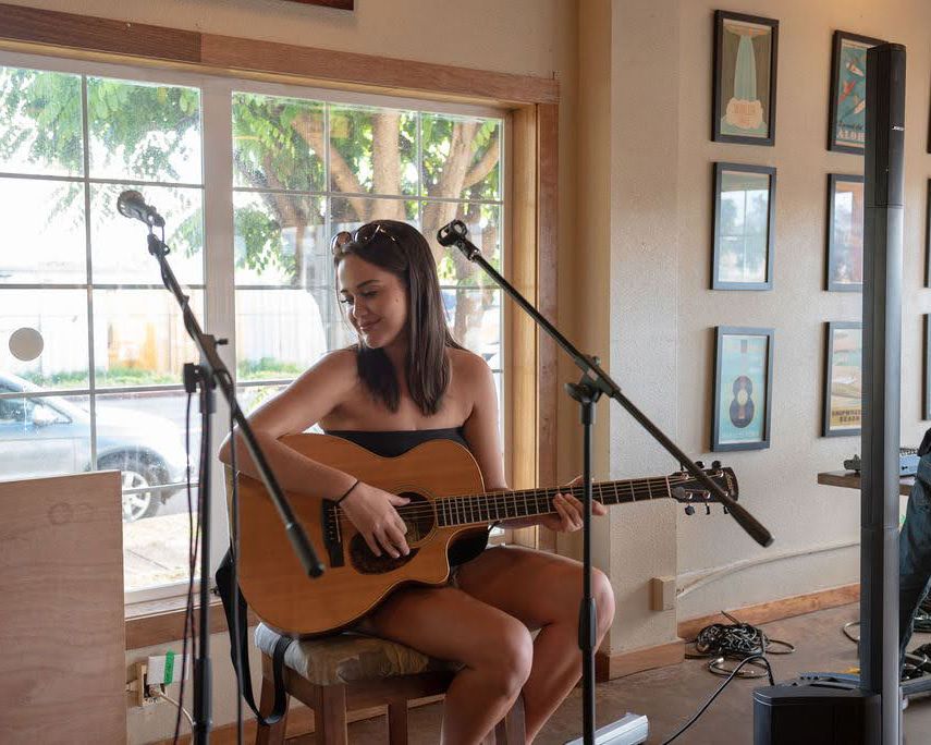 Musician performing with acoustic guitar in front of window with recording equipment.