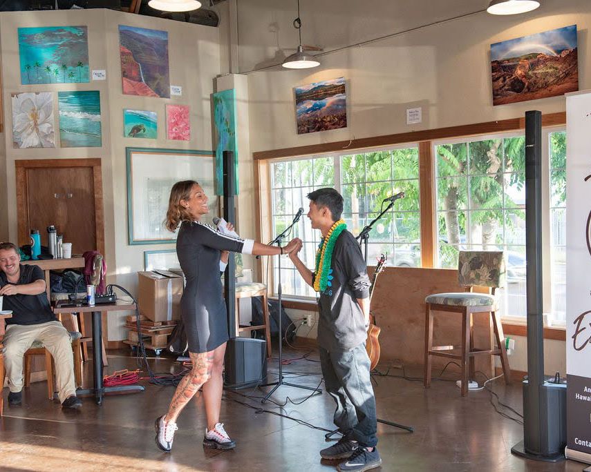 Two artists perform together in a bright cafe space decorated with colorful wall art and large windows.