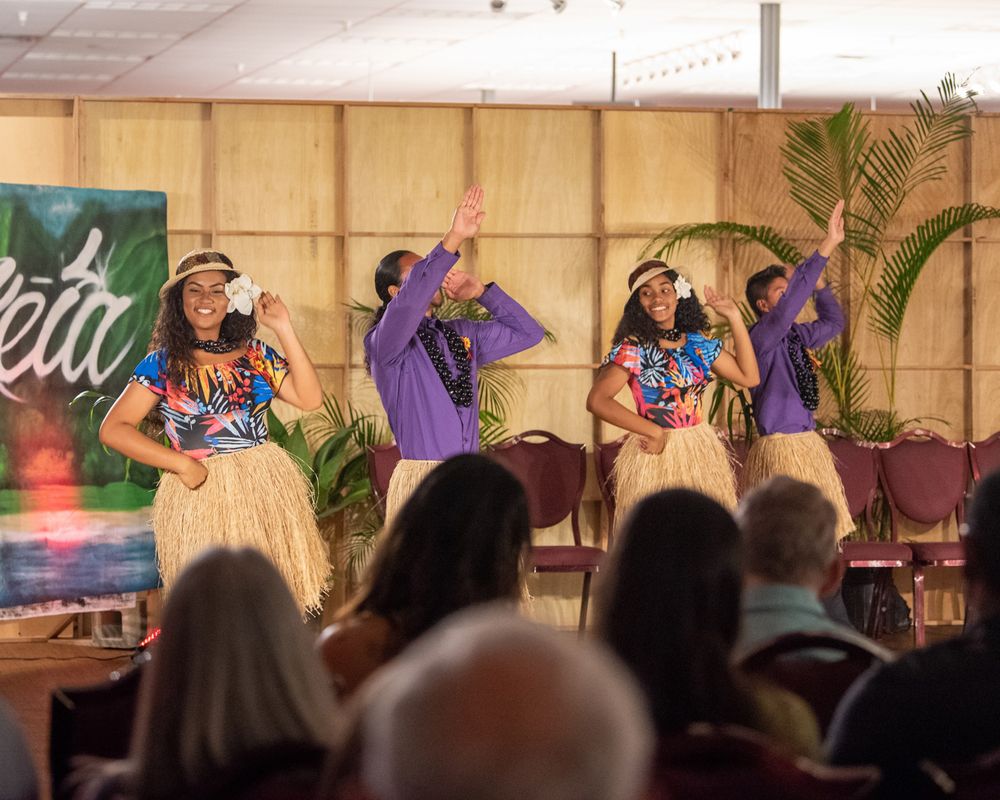 Hula dancers perform in traditional grass skirts on stage at a Hawaiian cultural show.
