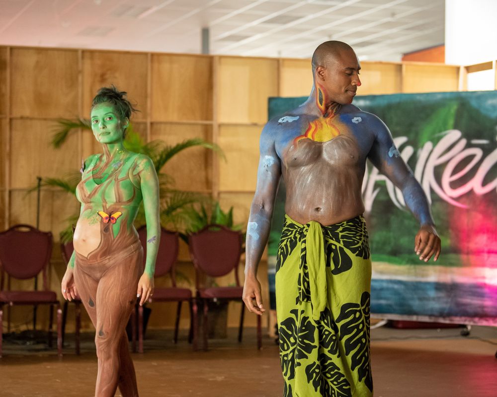 Two performers in body paint and traditional Hawaiian attire dance on stage during a cultural show.