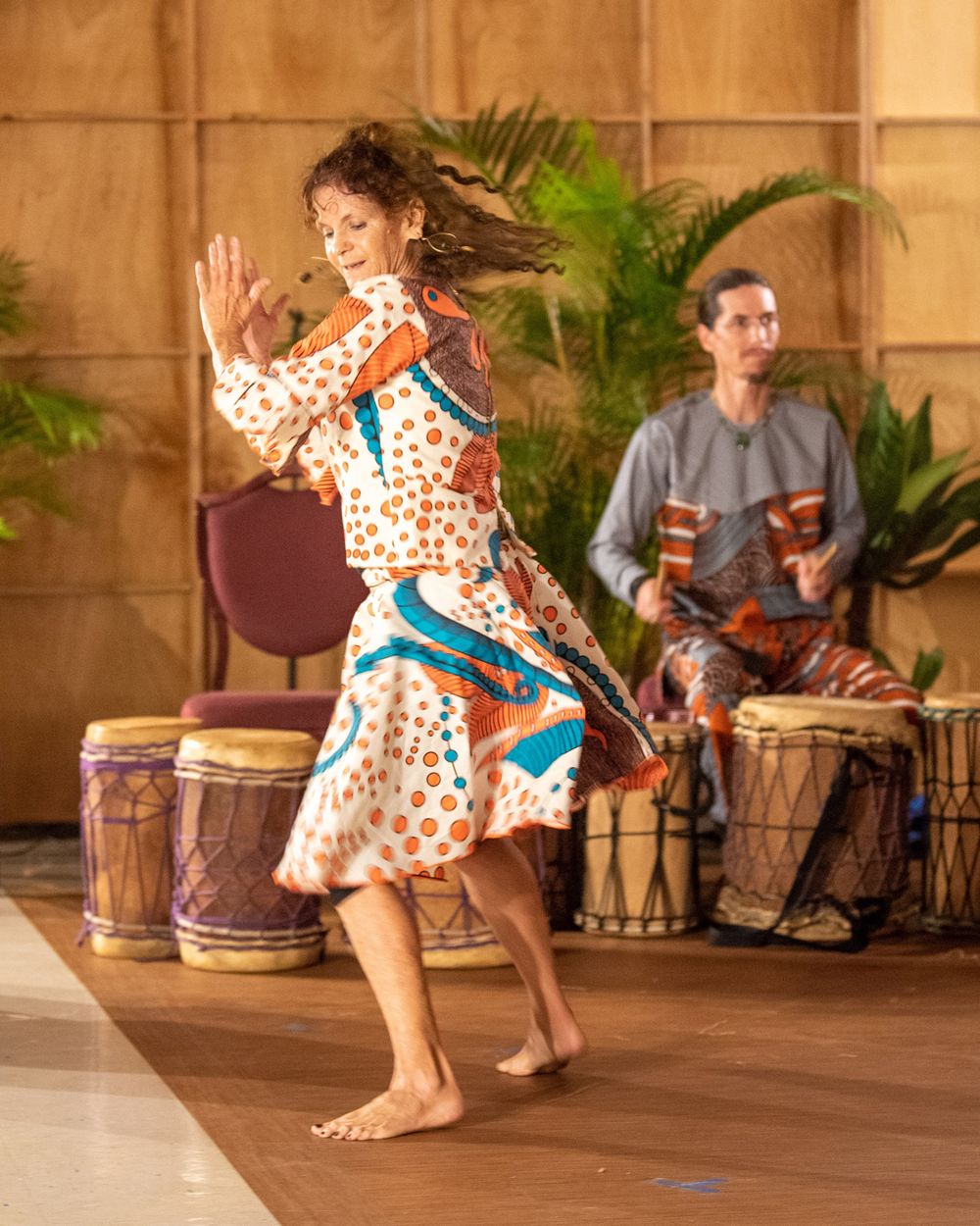 Dancer in patterned dress performs while drummer plays percussion in background.