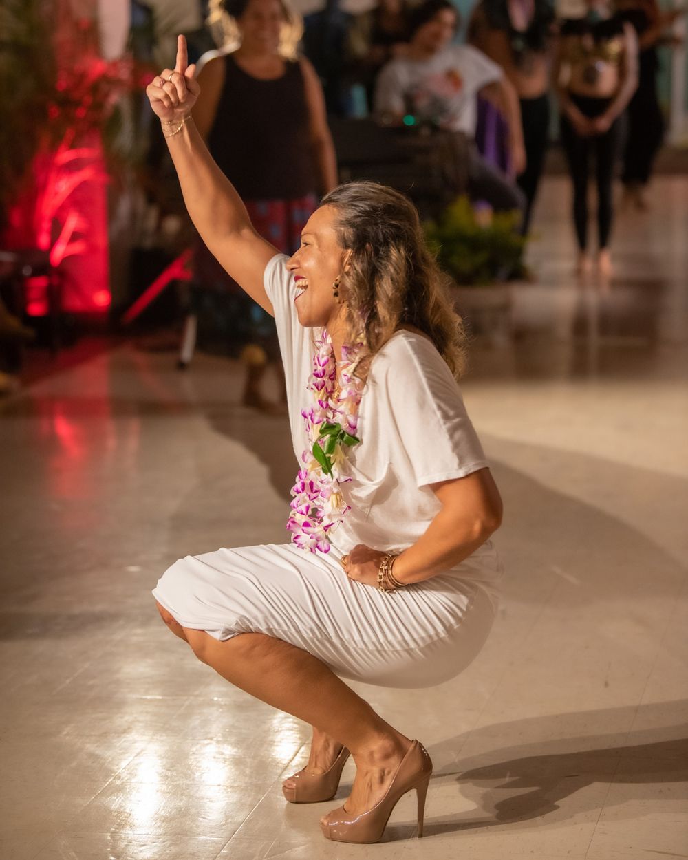 Dancer in white outfit strikes dynamic pose with raised arm on dance floor.