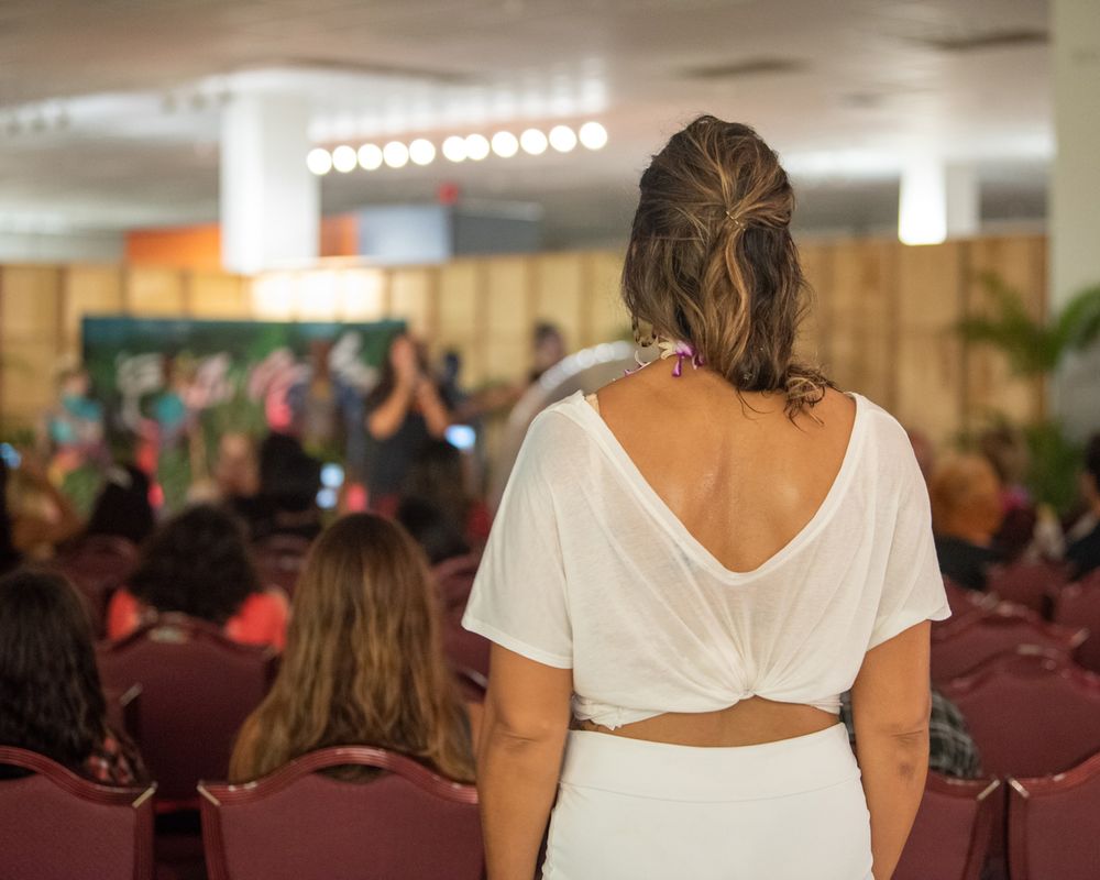 Back view of person in white outfit watching performance from audience.