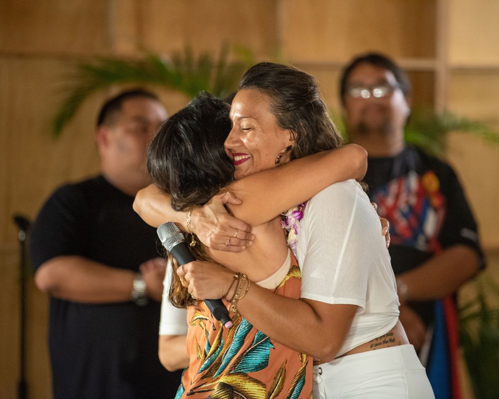 Two people share an emotional embrace during a special moment at an indoor event.