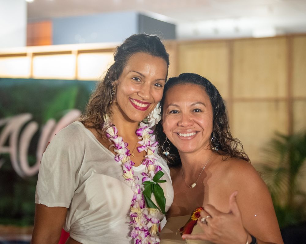 Two performers with flower leis pose together at tropical themed event.