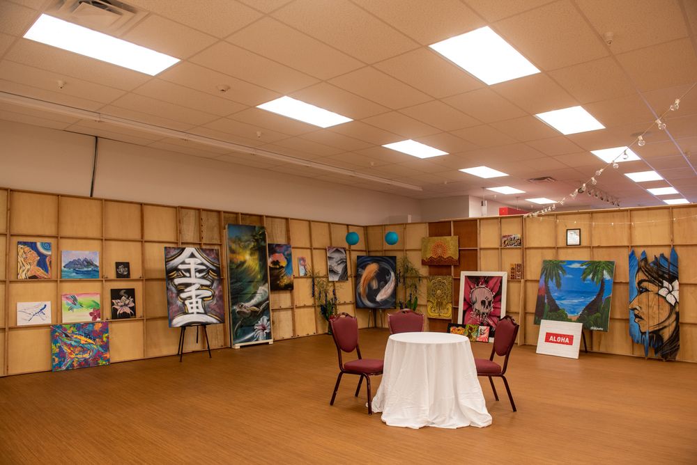 Empty event space with artwork displayed on walls and chairs arranged around a central table.