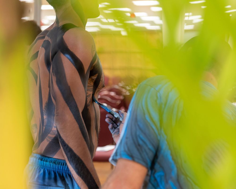 An artistic shot through green foliage showing tattooed figures in soft focus.
