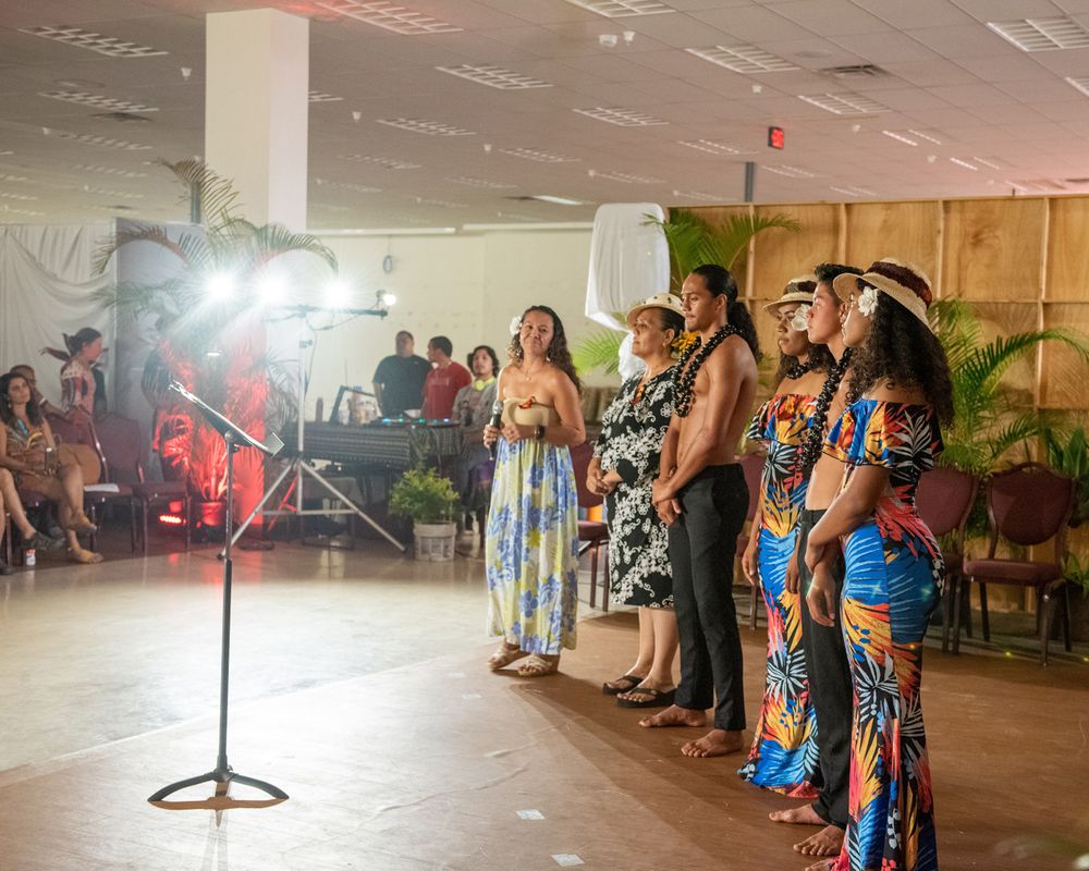 Performers line up on stage under bright lights during a cultural performance.