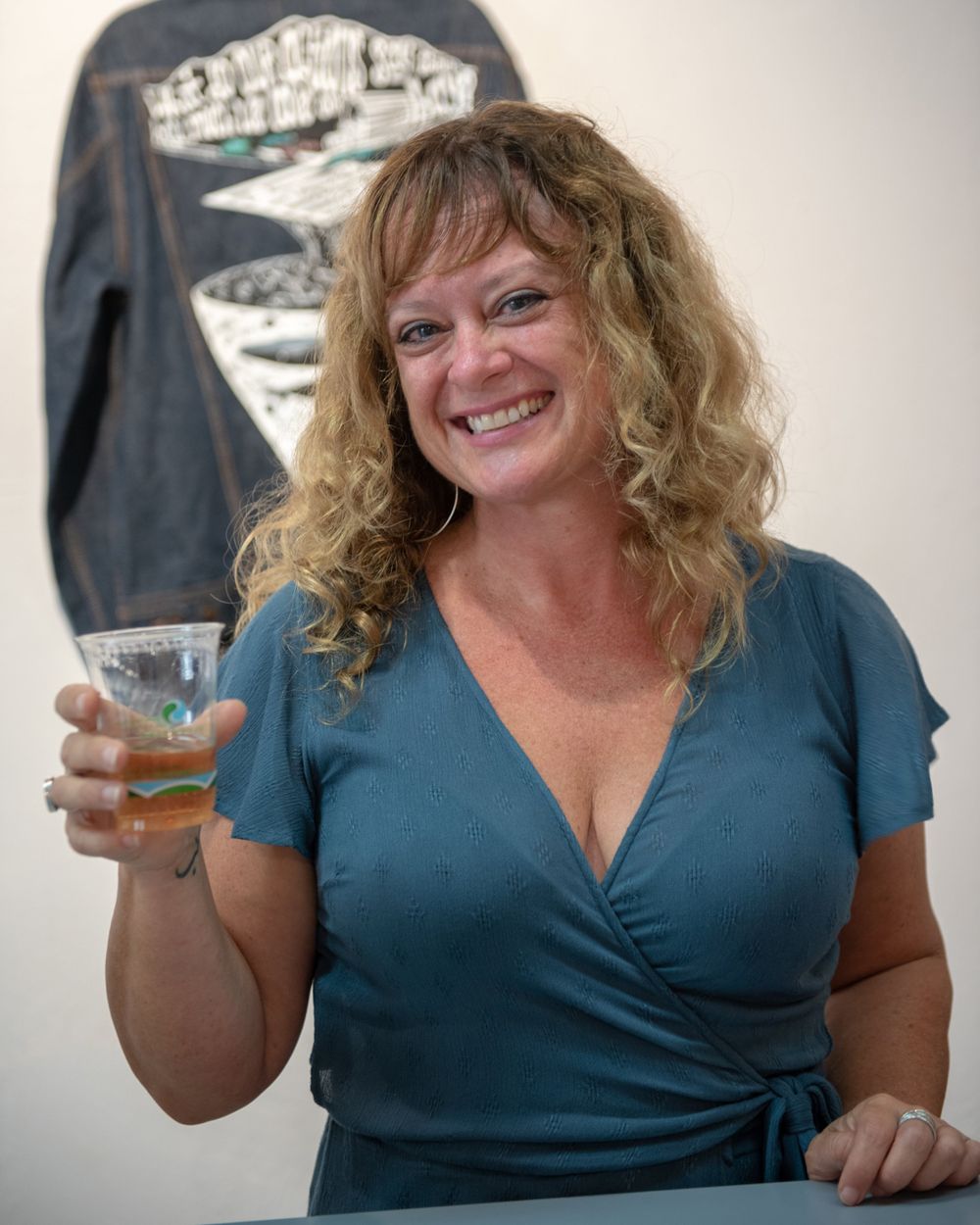 A person in a blue wrap dress holds up a cocktail while smiling warmly.