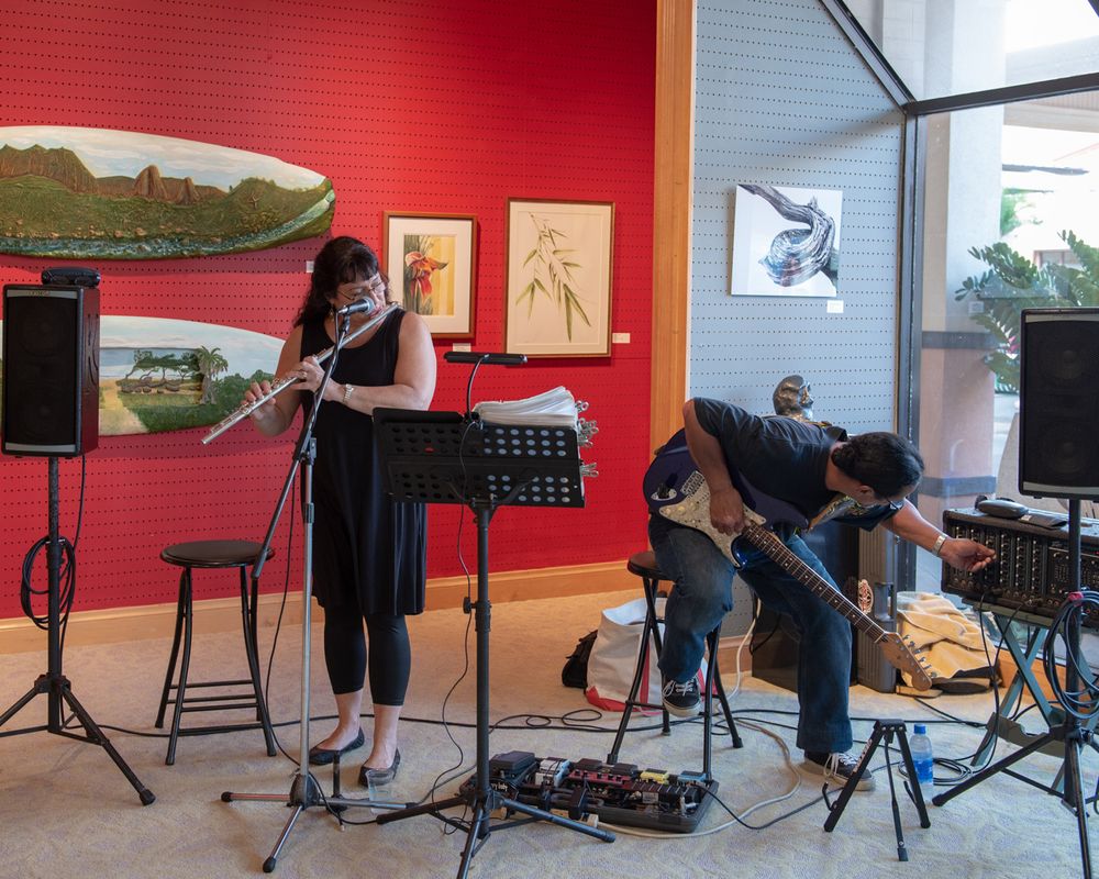 Musicians perform with instruments against a red wall backdrop in an art gallery.